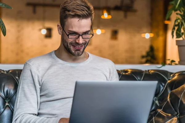 Foto dalam ruangan pemuda yang duduk di meja kafe menggunakan laptop — Stok Foto