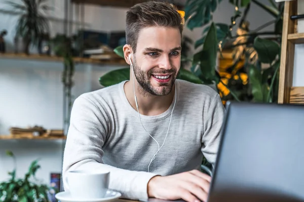 Jeune homme assis à la table de café en utilisant un ordinateur portable dans les écouteurs — Photo