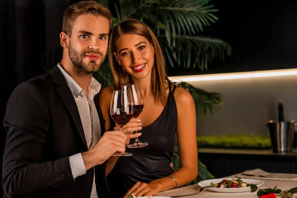 Porträt eines glücklichen Paares beim romantischen Abendessen, das mit Wein anstößt und in die Kamera blickt — Stockfoto