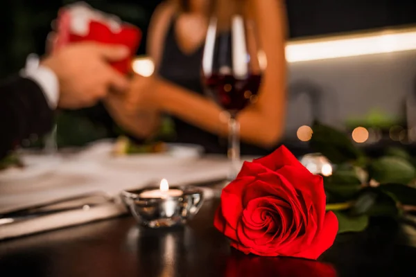 Junger Mann schenkt seiner Freundin eine Geschenkbox. Rose und Kerze im Vordergrund — Stockfoto