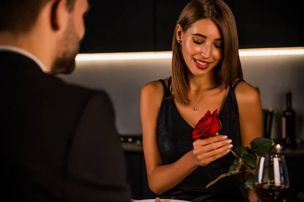 Young beautiful couple having romantic dinner at home. Attractive girl enjoys with rose from her boyfriend — Stock Photo, Image