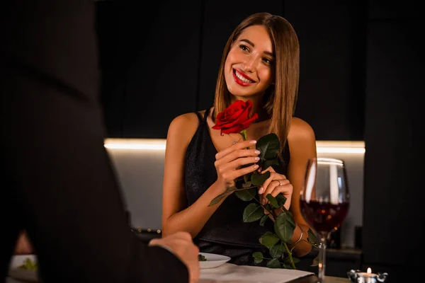 Szczęśliwa dziewczyna z różą w rękach patrząc na swojego chłopaka na randce — Zdjęcie stockowe