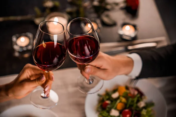 Primer plano de pareja joven brindando con copas de vino tinto en el restaurante Imagen de archivo