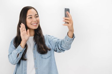 Asyalı güzel bir kadının portresi cep telefonu kullanıyor. Beyaz arka plan üzerinden video görüşmesi yaparken jest yapıyor.