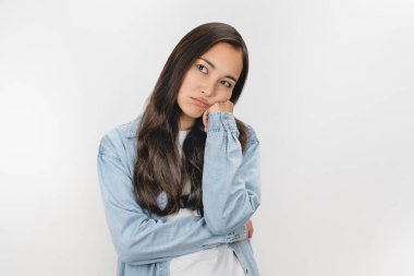 Genç ve güzel bir kadın üzgün görünüyor ve kollarını çapraz yapıp izole edilmiş beyaz arka planda sıkılıyor.