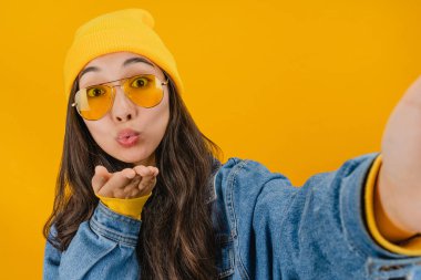 Sarı arka planda izole edilmiş akıllı telefondan, gülümseyen kadının selfie fotoğrafını çekerken yakın plan.