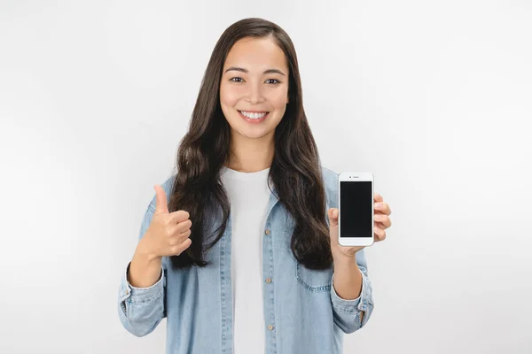 Feliz hermosa mujer joven sosteniendo la pantalla en blanco del teléfono móvil y levantando el pulgar sobre el fondo blanco — Foto de Stock