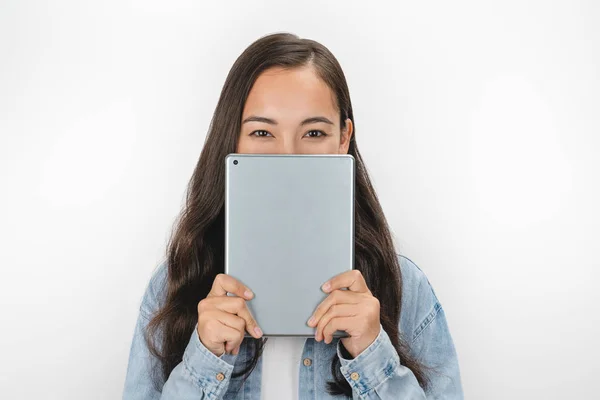 Retrato de niña cubriéndose la cara con una tableta digital de pie sobre una pared blanca — Foto de Stock