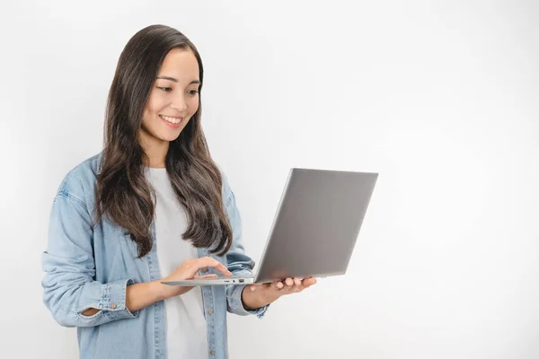 Junge glücklich lächelnde Frau in lässiger Kleidung hält Laptop in der Hand und sendet E-Mails vor weißem Hintergrund — Stockfoto