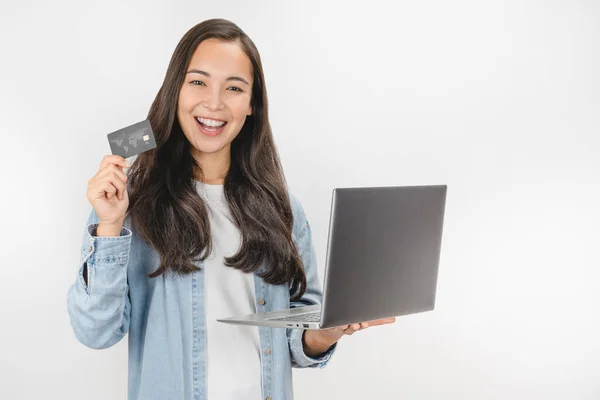 Portrait of happy woman in jeans shirt holding credit card and laptop isolated over white background — Stock Photo, Image