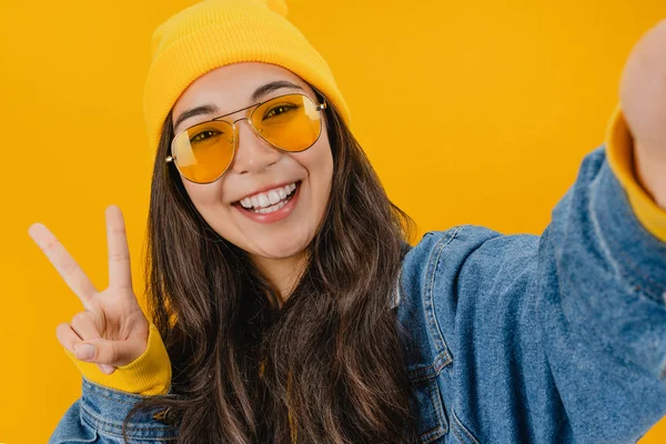 Χαρούμενη νεαρή κοπέλα δείχνει v-σημάδι λήψη selfie απομονώνονται σε κίτρινο φόντο — Φωτογραφία Αρχείου