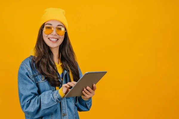 Портрет счастливой молодой азиатской девушки с помощью планшета на желтом фоне — стоковое фото