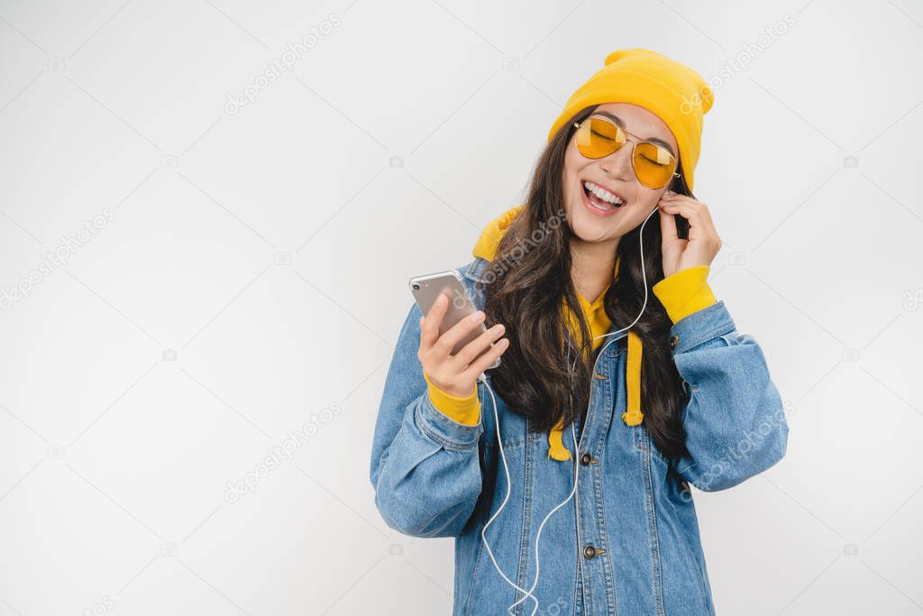 Image of young woman in hat posing isolated over white background listening music with earphones using mobile phone