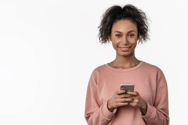 Porträtt av leende afrikansk ung kvinna stående och med mobiltelefon över vit bakgrund — Stockfoto