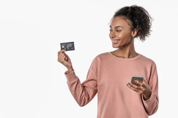 Smiling happy cheerful young pretty woman posing isolated over white wall background using mobile phone holding credit card — Stock Photo, Image