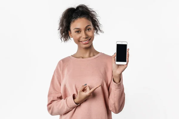 Usmívající se mladá žena drží mobilní telefon a ukazuje prstem přes bílé pozadí — Stock fotografie