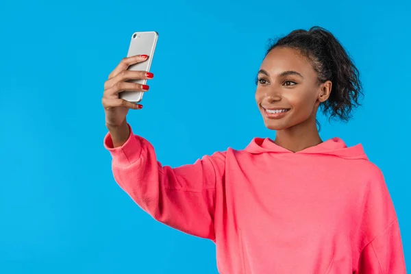 Mujer alegre haciendo selfie en el teléfono inteligente sobre fondo azul — Foto de Stock