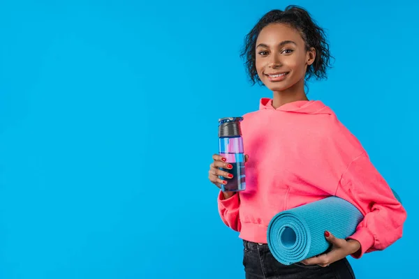 Mladý sport žena přes izolované modré pozadí se sportovní láhev vody a podložka — Stock fotografie