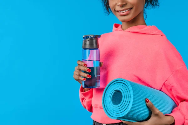 Imagem cortada de jovem mulher esporte sobre fundo azul isolado com esportes garrafa de água e tapete — Fotografia de Stock