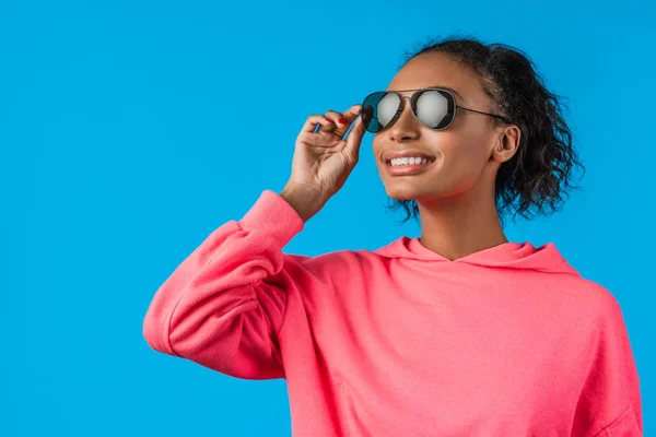 Linda modelo feminino afro-americano usar óculos de sol e posando sobre fundo azul — Fotografia de Stock