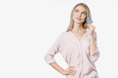 Sarışın bir kadının beyaz arka planda izole bir şekilde poz verdiğini ve elinde kredi kartı tuttuğunu düşünüyorum..