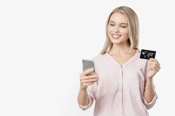 Smiling young lady isolated over white background using mobile phone holding credit card — Stock Photo, Image