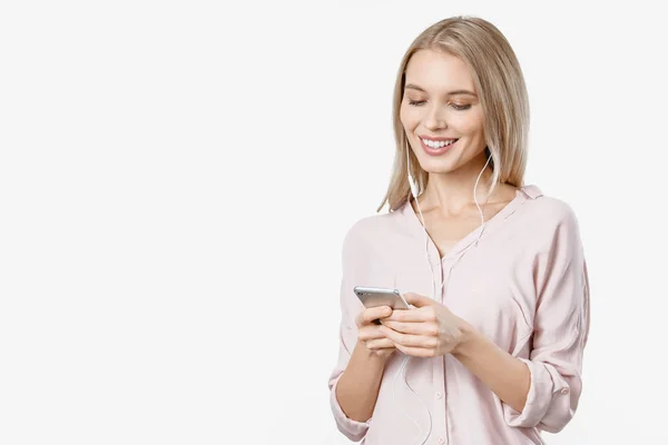 Glad ung vacker kvinna poserar isolerad över vit bakgrund lyssna musik med hörlurar och använda mobiltelefon. — Stockfoto
