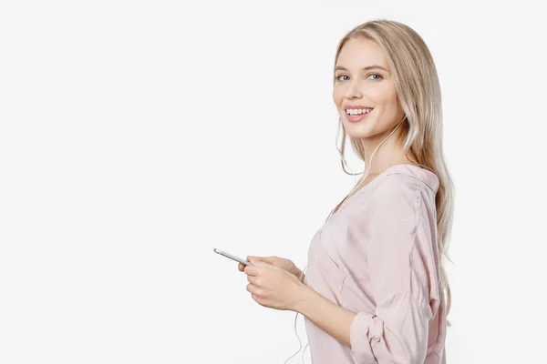 Hermosa mujer escuchando música con auriculares y utilizando el teléfono móvil posando aislado sobre fondo blanco — Foto de Stock