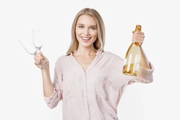Όμορφη νεαρή ξανθιά κοπέλα γιορτάζει με μπουκάλι σαμπάνια και δύο ποτήρια στέκεται απομονωμένη πάνω από λευκό φόντο — Φωτογραφία Αρχείου