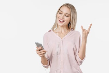 Cep telefonu ve kulaklıklı müzik dinleyen genç bir kadın izole edilmiş beyaz arka planda rock hareketi yapıyor.