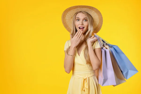 Portré megdöbbent lány ruha gazdaság bevásárló táskák és nézi a kamera elszigetelt sárga háttér — Stock Fotó