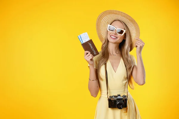 Touristin lächelt, während sie Retro-Kamera und Reisetickets isoliert vor gelbem Hintergrund hält — Stockfoto