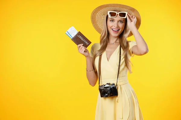 Überraschte Touristin mit Retro-Kamera und Reisetickets vor gelbem Hintergrund — Stockfoto