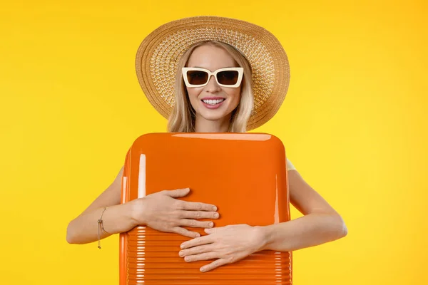 Fiatal lány kalap és napszemüveg nyaralás utazási bőrönddel izolált sárga háttér — Stock Fotó