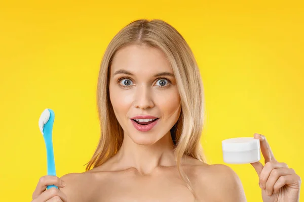 Mujer hermosa sorprendida sosteniendo crema de piel sobre fondo amarillo — Foto de Stock