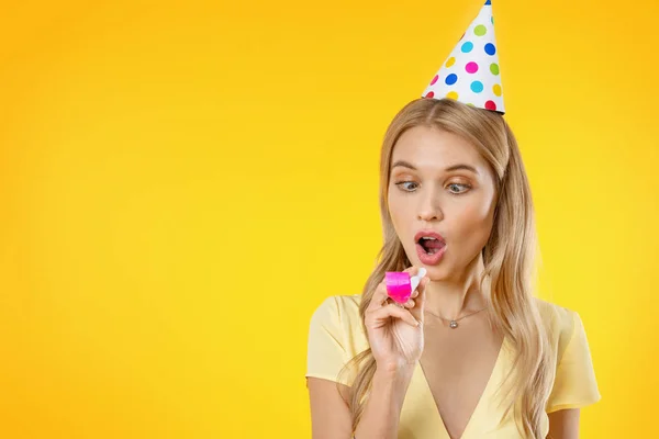 Mulher feliz se divertindo no chapéu de festa de aniversário jogando cachimbo sobre fundo amarelo — Fotografia de Stock