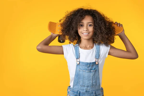 快乐的十多岁女孩，肩膀上挂着滑板，背景是黄色的 — 图库照片