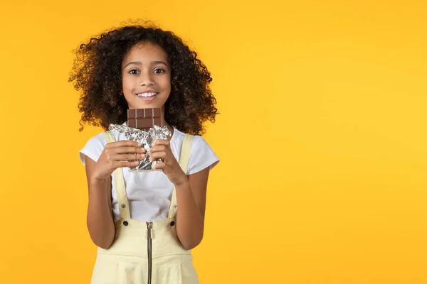 Liten afro flicka äter choklad isolerad på gul bakgrund — Stockfoto