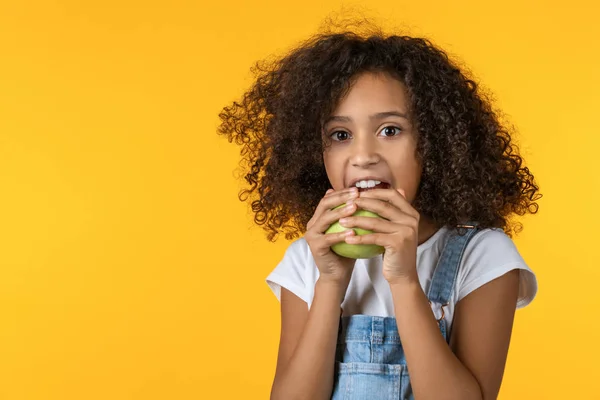 Menina comendo maçã sobre fundo amarelo — Fotografia de Stock