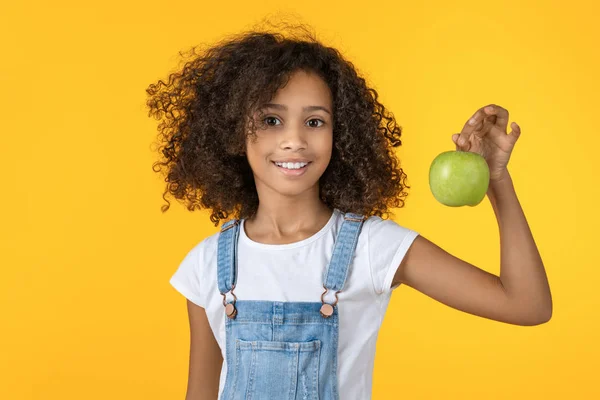 Menina africana bonito segurando maçã verde isolado no fundo amarelo . — Fotografia de Stock