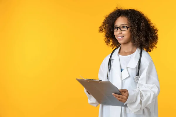 Carino bambina vestita come medico con blocco note isolato su sfondo giallo — Foto Stock