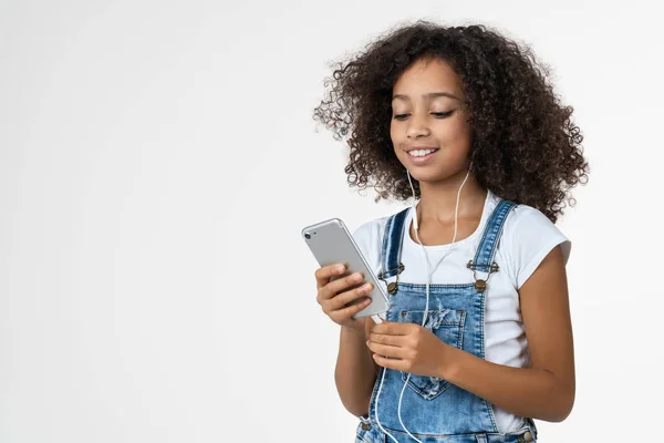 Beyaz arka planda izole edilmiş akıllı telefon ve kulaklık kullanırken gülümseyen mutlu Afrikalı Amerikalı kız. — Stok fotoğraf