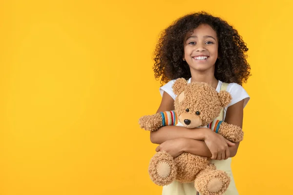 Retrato de niña africana sonriente abrazando juguete oso de peluche aislado sobre fondo amarillo — Foto de Stock