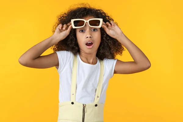 Chica joven con gafas de sol en shock con una cara sorpresa aislada sobre fondo amarillo — Foto de Stock