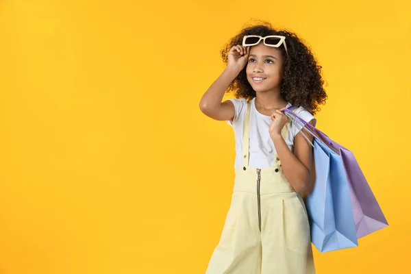 Счастливая девочка с сумкой в руках на желтом фоне в студии — стоковое фото