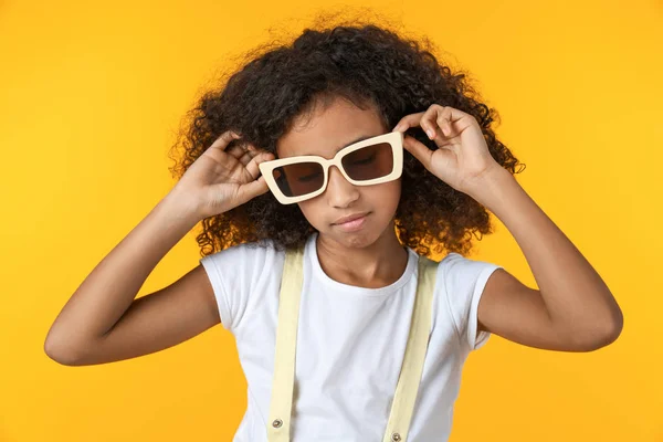 Молодая красивая кудрявая девушка в солнечных очках выглядит скучно на изолированном желтом фоне — стоковое фото
