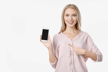 Gülümseyen bir kadın akıllı telefonu işaret ederek beyaz arka grubunda duruyor.