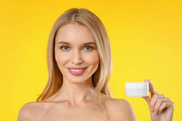 Retrato de mujer hermosa sosteniendo crema de piel sobre fondo amarillo — Foto de Stock