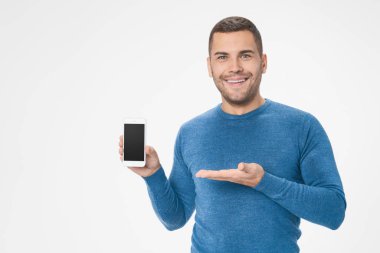 Shot of man in blue sweater presenting smart phone with black screen with copyspace isolated on white background