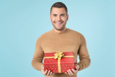 Handsome man in casuals with gift box isolated on blue background